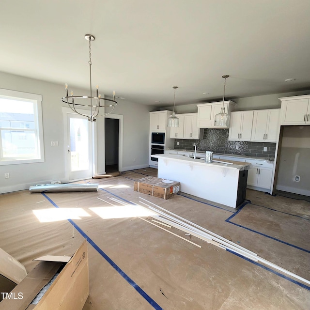 kitchen featuring hanging light fixtures, a notable chandelier, an island with sink, and white cabinetry