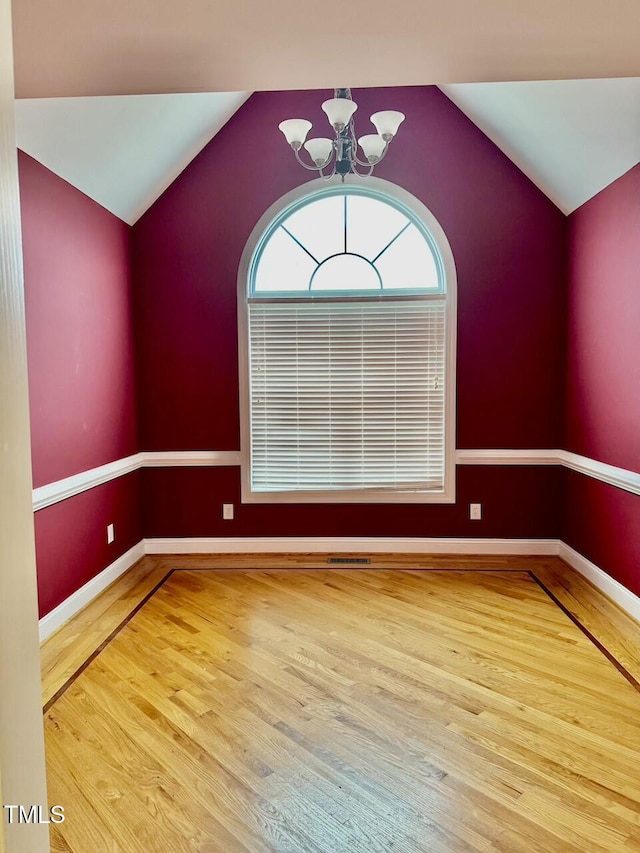 empty room featuring lofted ceiling, an inviting chandelier, and hardwood / wood-style flooring