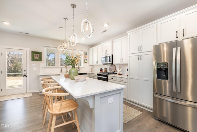 kitchen with light stone countertops, a center island, decorative light fixtures, white cabinetry, and stainless steel appliances