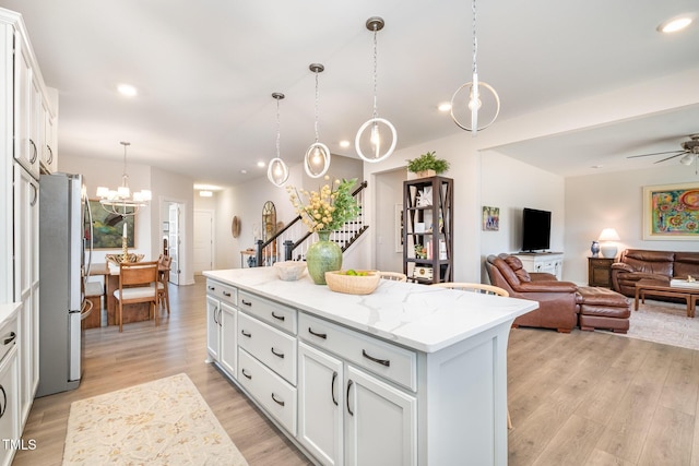 kitchen featuring white cabinetry, stainless steel fridge, decorative light fixtures, light stone countertops, and a center island