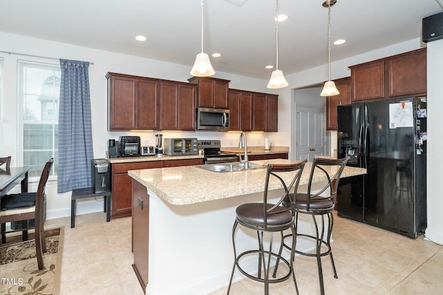 kitchen featuring appliances with stainless steel finishes, sink, hanging light fixtures, a kitchen island with sink, and light stone counters