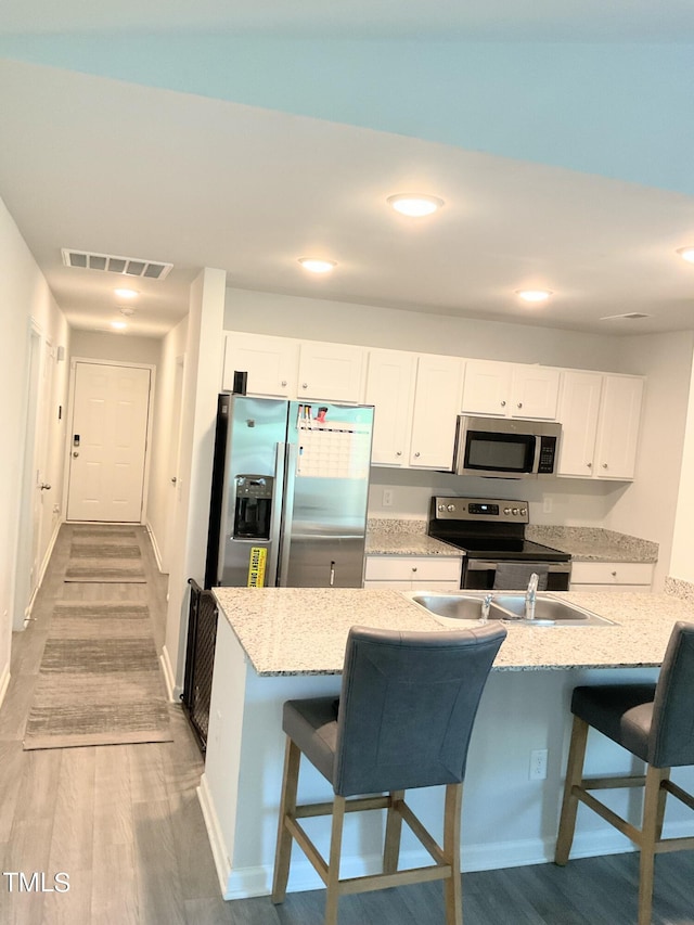 kitchen featuring light hardwood / wood-style floors, appliances with stainless steel finishes, a kitchen breakfast bar, white cabinets, and light stone counters