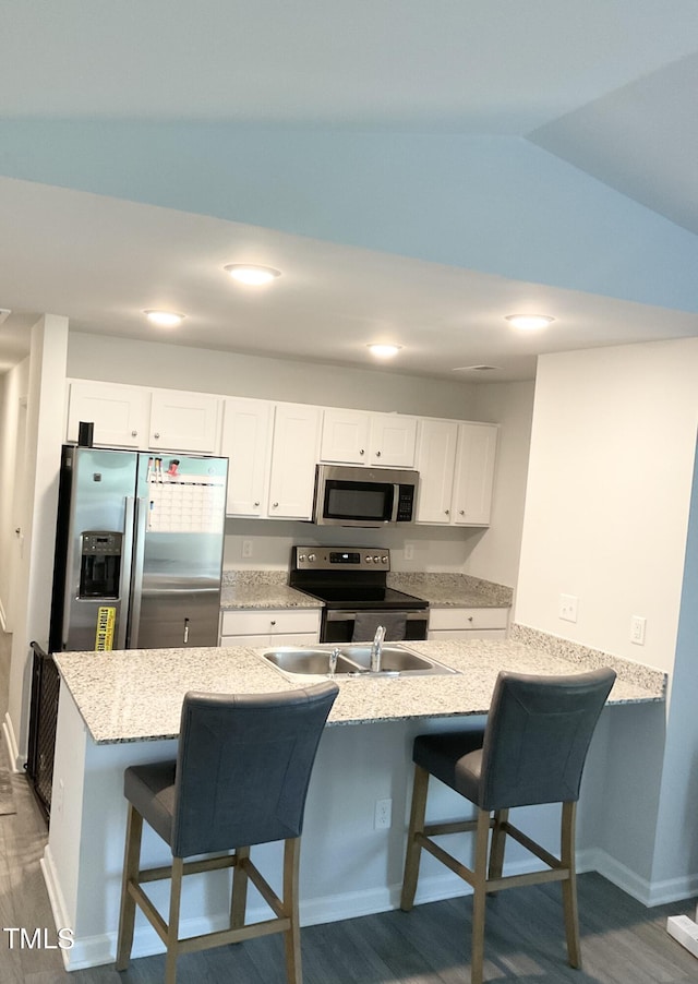 kitchen featuring a kitchen bar, white cabinets, appliances with stainless steel finishes, and vaulted ceiling