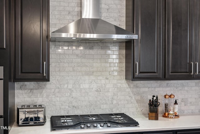 kitchen with backsplash, light countertops, stainless steel gas cooktop, and wall chimney range hood