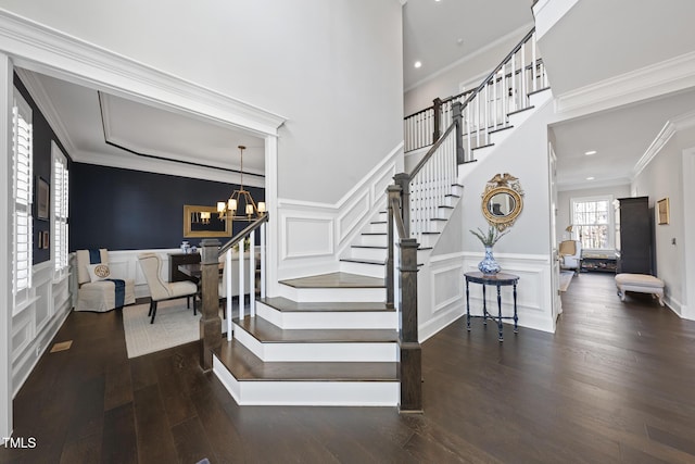 stairway with a decorative wall, a wainscoted wall, wood finished floors, an inviting chandelier, and crown molding