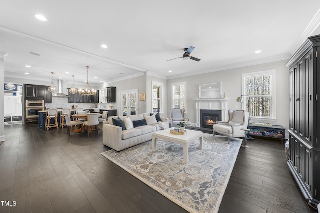 living room featuring a healthy amount of sunlight, dark wood-style floors, crown molding, and a glass covered fireplace