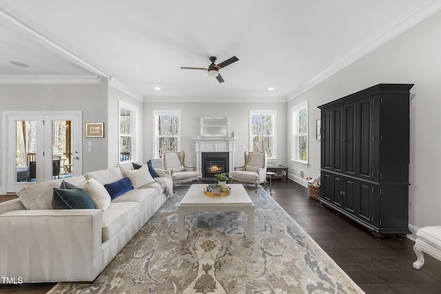 living room featuring dark wood-style floors, a glass covered fireplace, crown molding, and baseboards