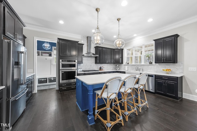 kitchen featuring a kitchen island, appliances with stainless steel finishes, ornamental molding, light countertops, and wall chimney range hood