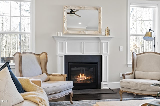 sitting room featuring dark wood-type flooring, a glass covered fireplace, and baseboards