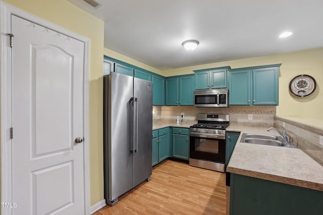 kitchen with sink, light hardwood / wood-style flooring, blue cabinetry, appliances with stainless steel finishes, and decorative backsplash