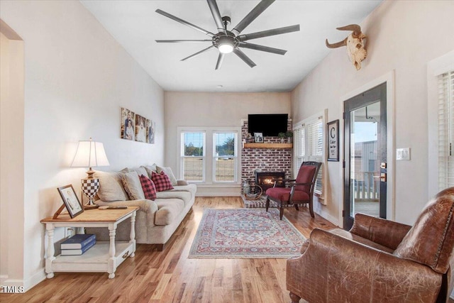 living room featuring a brick fireplace, light hardwood / wood-style flooring, and ceiling fan