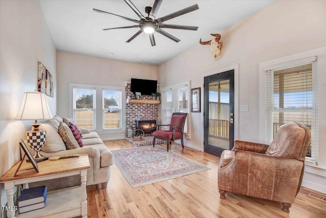 living room featuring ceiling fan, light wood-type flooring, and a fireplace