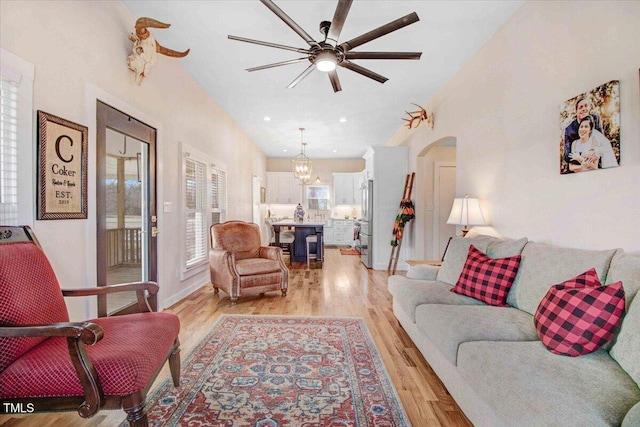 living room with light wood-type flooring and ceiling fan with notable chandelier