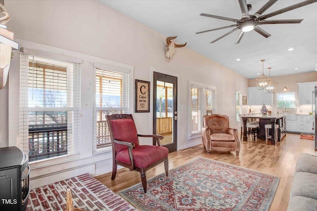 living room featuring light wood-type flooring, lofted ceiling, and ceiling fan with notable chandelier