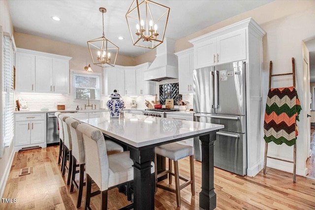 kitchen featuring premium range hood, a center island, white cabinetry, a breakfast bar area, and stainless steel appliances