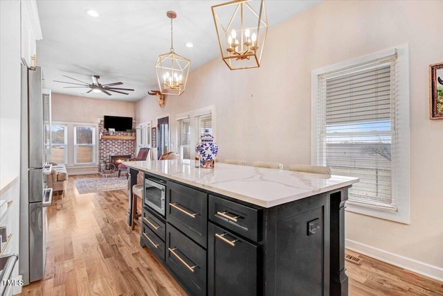 kitchen with a center island, decorative light fixtures, white cabinetry, a brick fireplace, and light hardwood / wood-style flooring