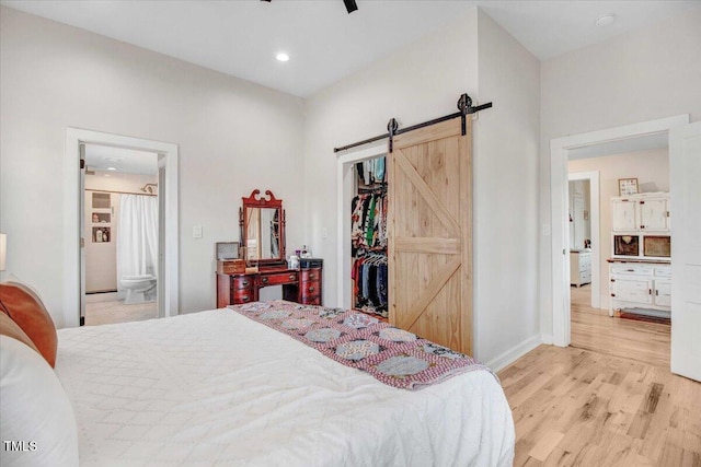 bedroom featuring ensuite bath, a closet, ceiling fan, light hardwood / wood-style flooring, and a barn door