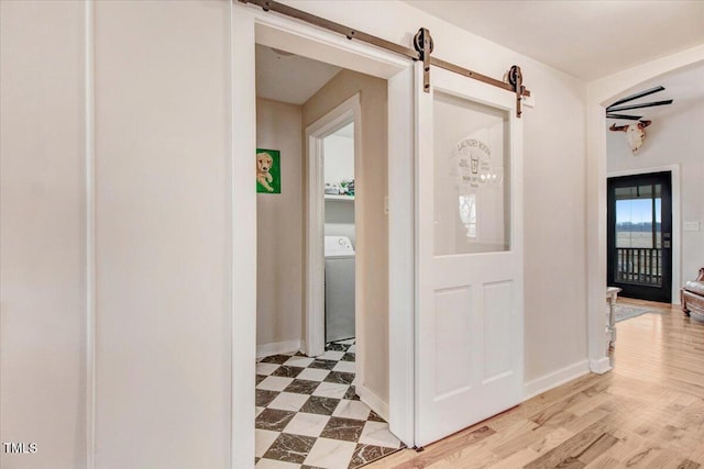 hall with washer / dryer, a barn door, and light hardwood / wood-style flooring