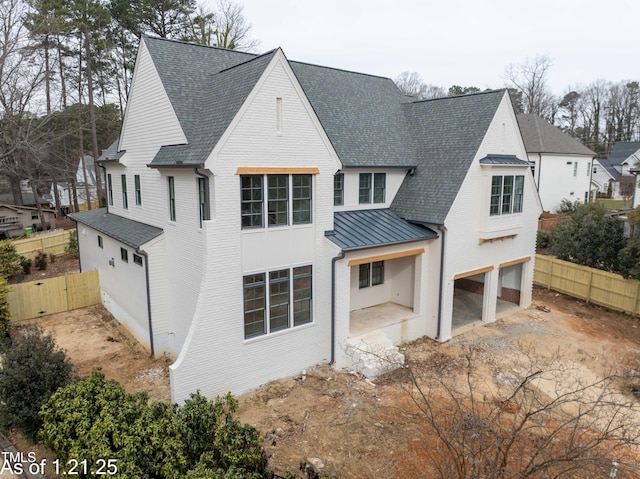 view of front facade with a standing seam roof, fence, driveway, and a patio