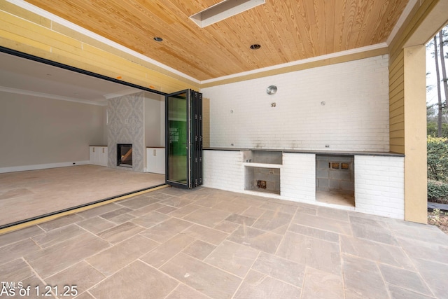 unfurnished living room with brick wall, wood ceiling, a fireplace, and ornamental molding