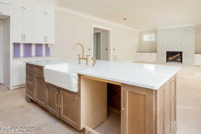 kitchen with a premium fireplace, ornamental molding, white cabinetry, a sink, and an island with sink