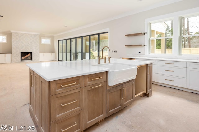 kitchen with ornamental molding, a kitchen island with sink, light countertops, a fireplace, and a sink