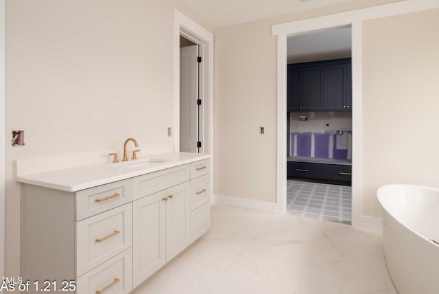 bathroom with marble finish floor, vanity, baseboards, and a soaking tub