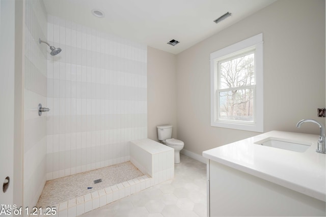 bathroom with toilet, vanity, baseboards, a tile shower, and tile patterned floors