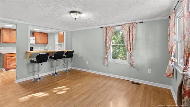 kitchen featuring a kitchen bar, kitchen peninsula, crown molding, a textured ceiling, and light wood-type flooring