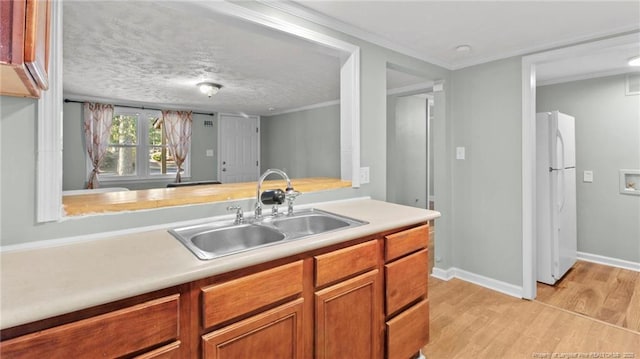 kitchen with brown cabinets, light countertops, light wood-style flooring, freestanding refrigerator, and a sink