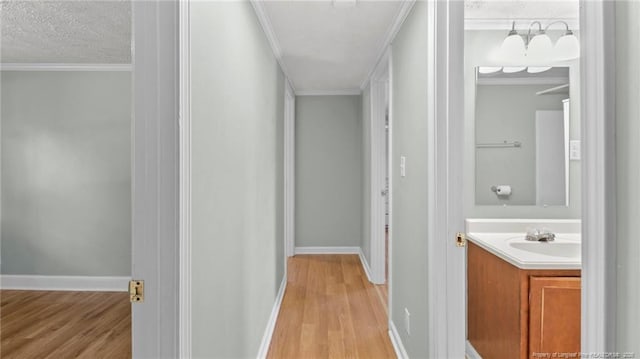 hall with light wood-type flooring, crown molding, a textured ceiling, and baseboards