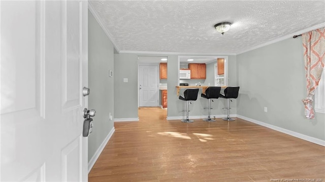 interior space featuring crown molding, a textured ceiling, baseboards, and light wood-style floors