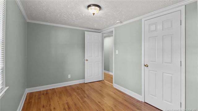 unfurnished bedroom with baseboards, light wood finished floors, a textured ceiling, and crown molding