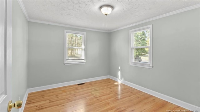 empty room with a textured ceiling, wood finished floors, visible vents, baseboards, and crown molding