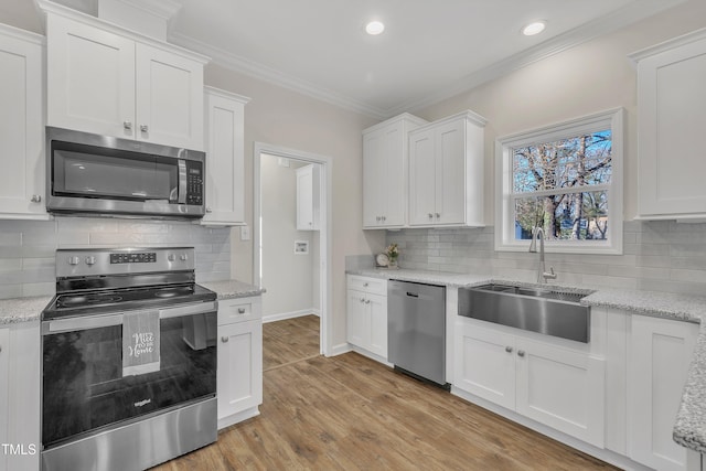 kitchen with white cabinetry, stainless steel appliances, light hardwood / wood-style floors, sink, and ornamental molding