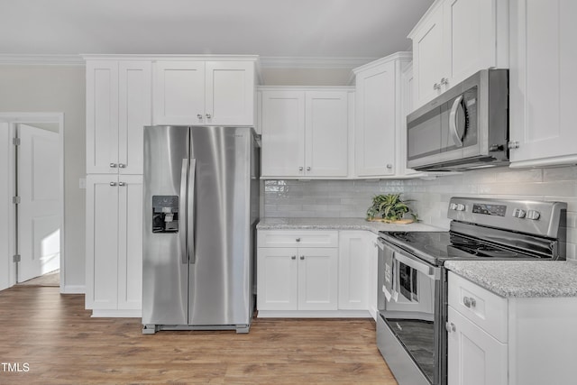 kitchen with white cabinets, stainless steel appliances, light stone counters, light hardwood / wood-style flooring, and crown molding