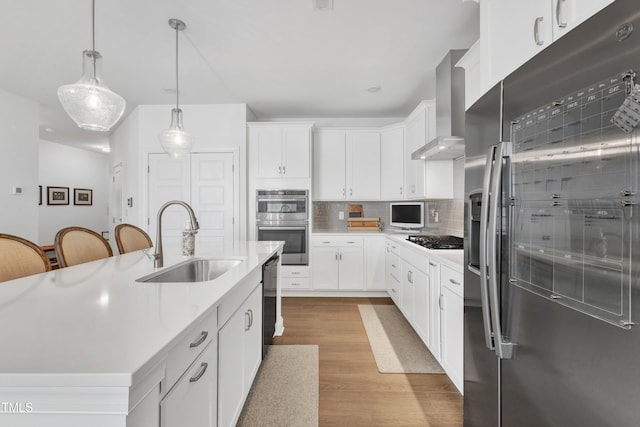 kitchen featuring sink, white cabinetry, a kitchen island with sink, appliances with stainless steel finishes, and wall chimney exhaust hood