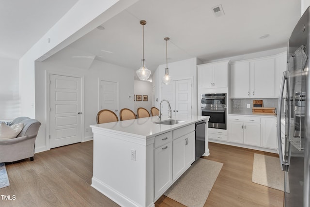 kitchen featuring sink, pendant lighting, white cabinets, and a center island with sink