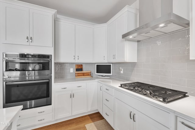 kitchen featuring light hardwood / wood-style floors, stainless steel appliances, backsplash, wall chimney range hood, and white cabinets