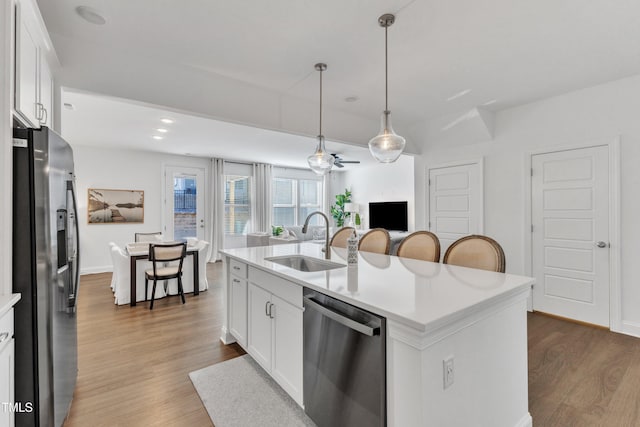 kitchen featuring decorative light fixtures, sink, white cabinetry, appliances with stainless steel finishes, and an island with sink