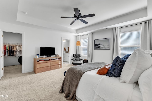 bedroom with a spacious closet, connected bathroom, a closet, ceiling fan, and a tray ceiling