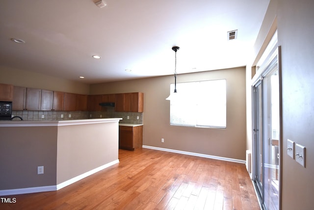 kitchen with black microwave, light hardwood / wood-style floors, backsplash, and decorative light fixtures