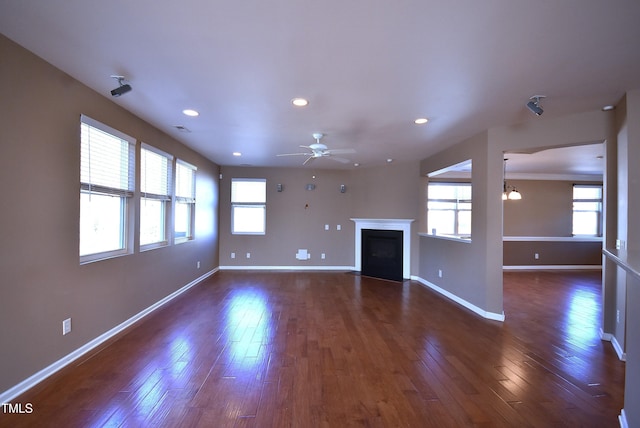 unfurnished living room featuring ceiling fan, a healthy amount of sunlight, and dark hardwood / wood-style flooring