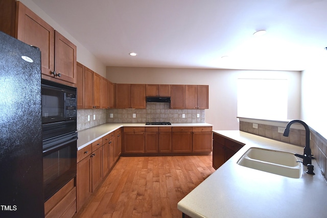 kitchen with light wood-type flooring, sink, tasteful backsplash, and black appliances