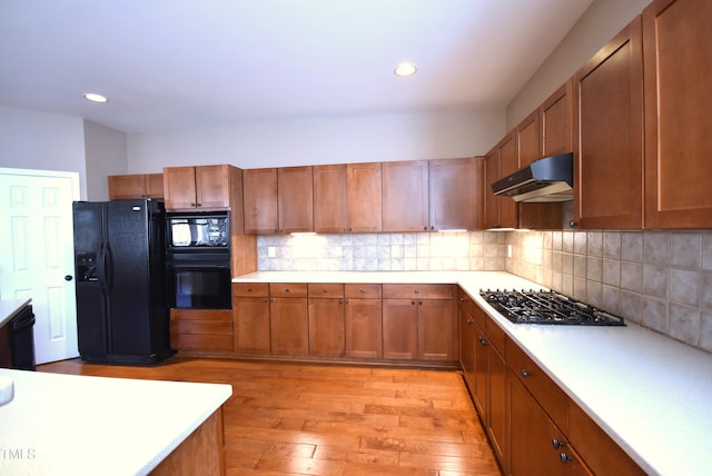 kitchen with decorative backsplash, black appliances, and light wood-type flooring