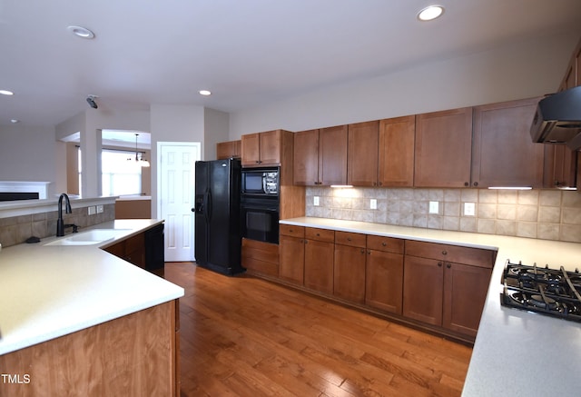 kitchen with black appliances, wood-type flooring, sink, backsplash, and range hood