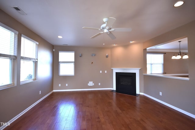 unfurnished living room with ceiling fan with notable chandelier, dark hardwood / wood-style floors, and a healthy amount of sunlight