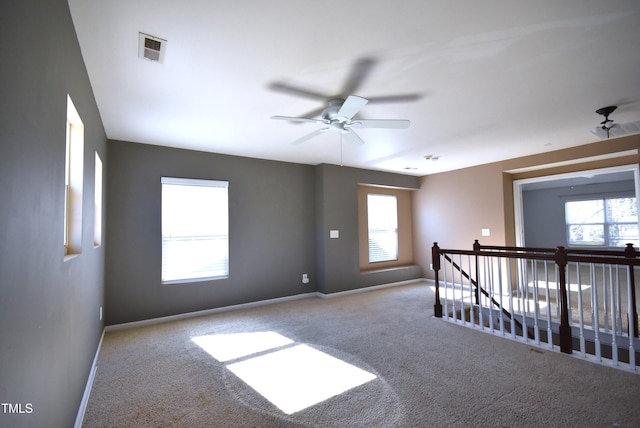 empty room featuring ceiling fan, light colored carpet, and a wealth of natural light