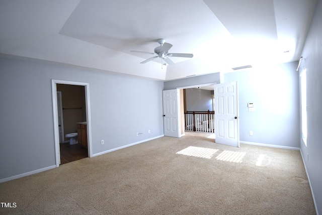 unfurnished bedroom with light colored carpet, a raised ceiling, and ensuite bath