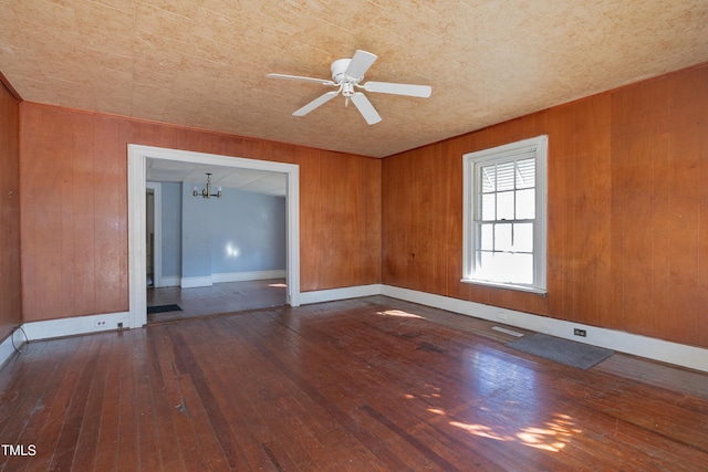 unfurnished room featuring ceiling fan with notable chandelier, hardwood / wood-style flooring, and wooden walls